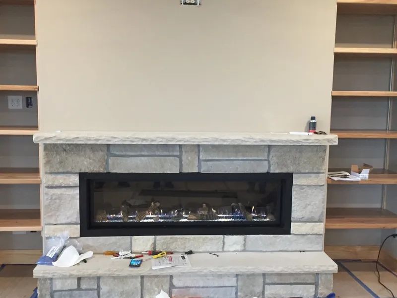Stone fireplace with black insert between built-in shelves, tools on hearth in a room under renovation