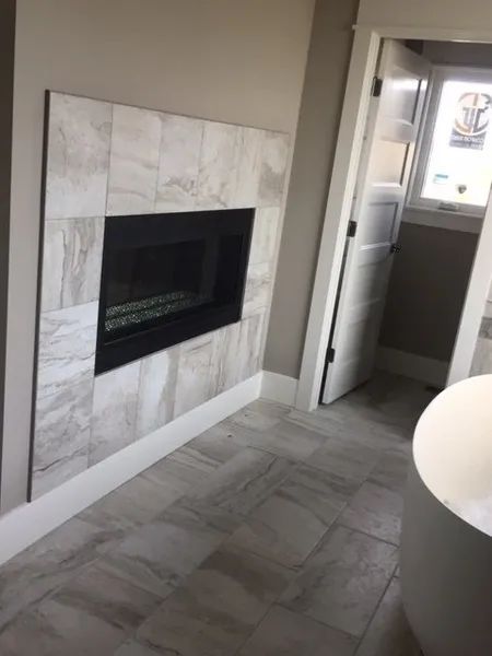 Modern room with a marble fireplace and tiled floor, next to an open doorway and window.