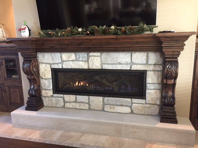 Stone fireplace with a lit fire, dark wood mantel, and decorative columns in a living room