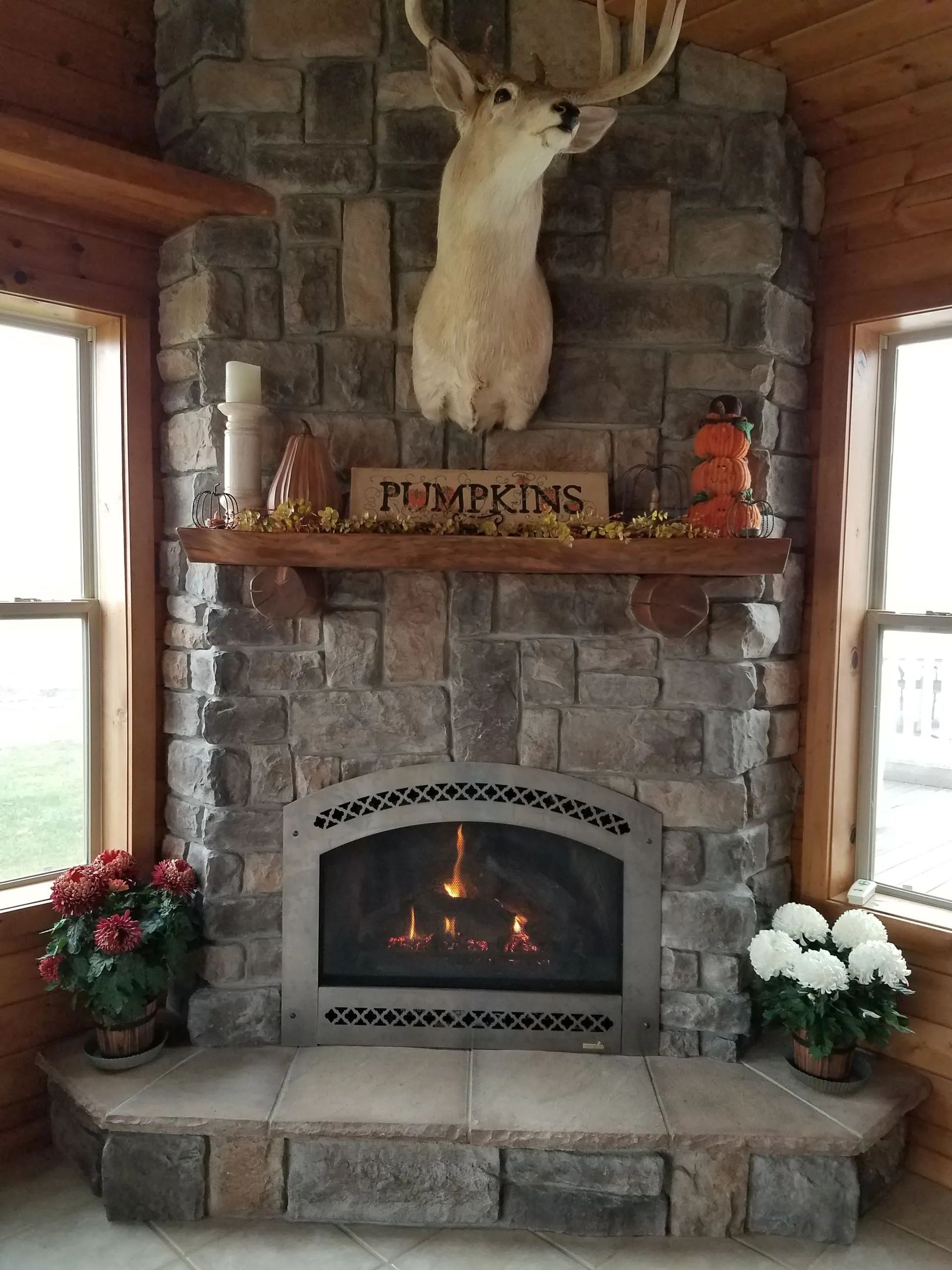 Rustic stone fireplace with mounted deer head, autumn decor, and flowers on the hearth