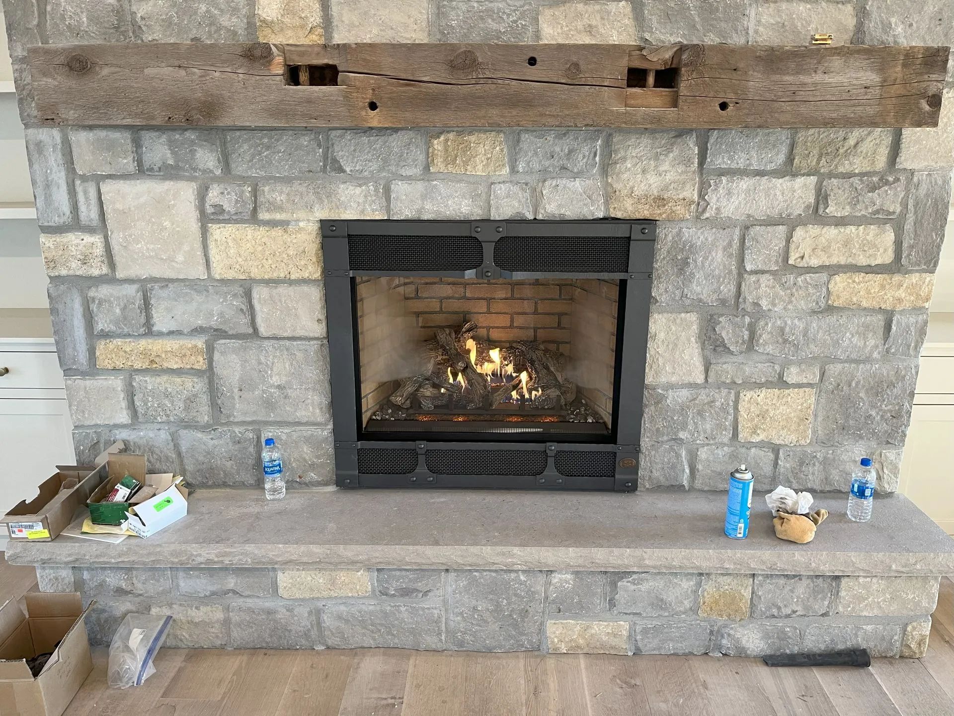 Stone fireplace with a lit fire, wooden mantel, and small items on the hearth.