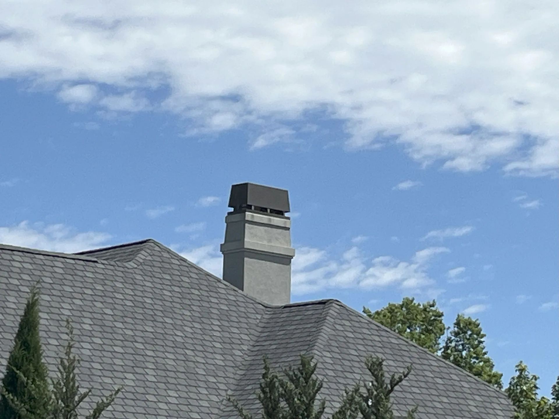 Gray house roof with a chimney under a blue sky with clouds