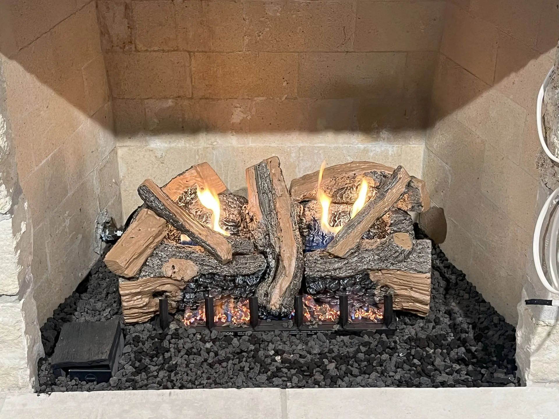 Lit gas fireplace with logs and bright flames inside a brown brick hearth