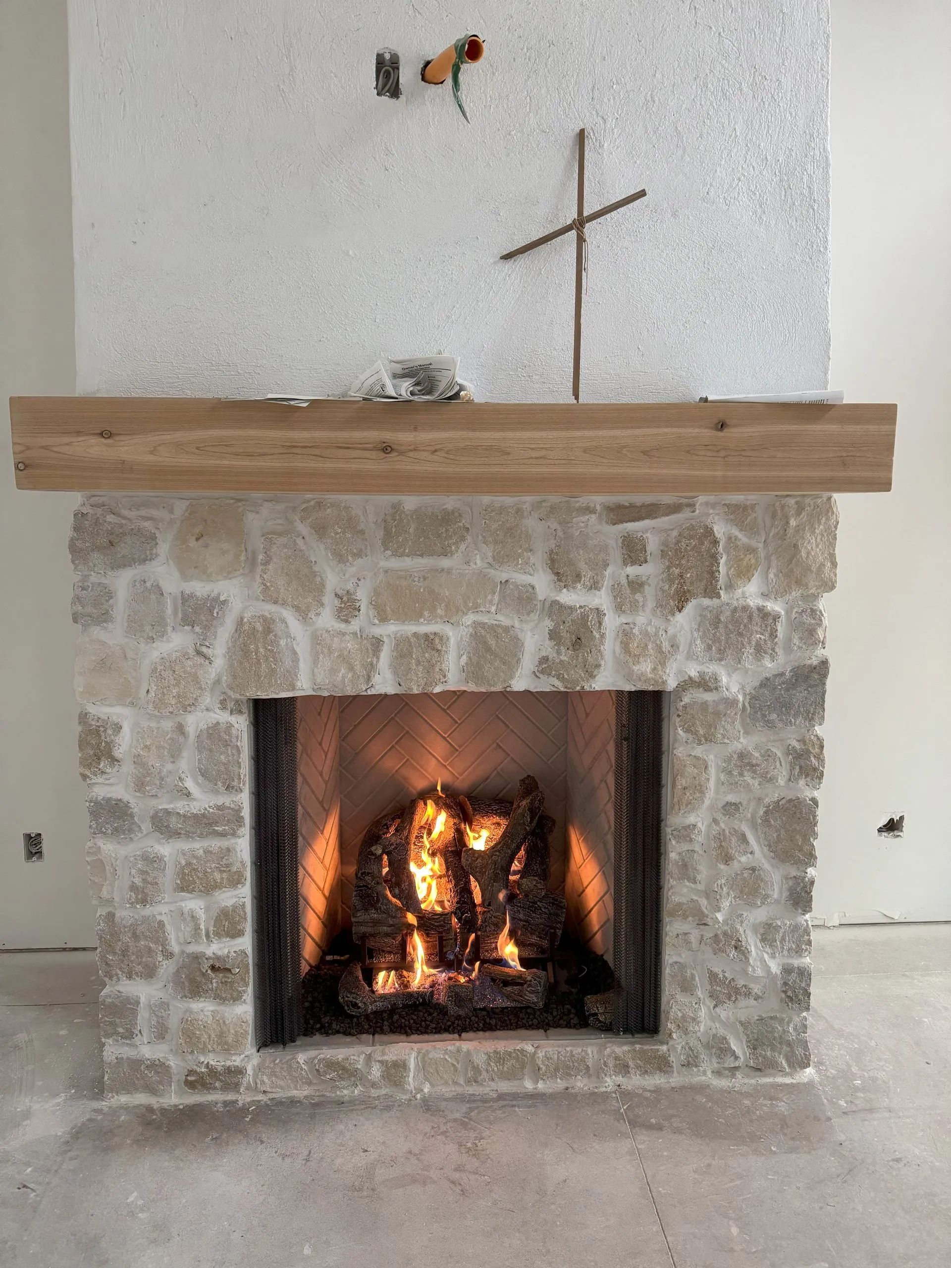 Stone fireplace with a lit fire and wooden mantel in a room with white walls.