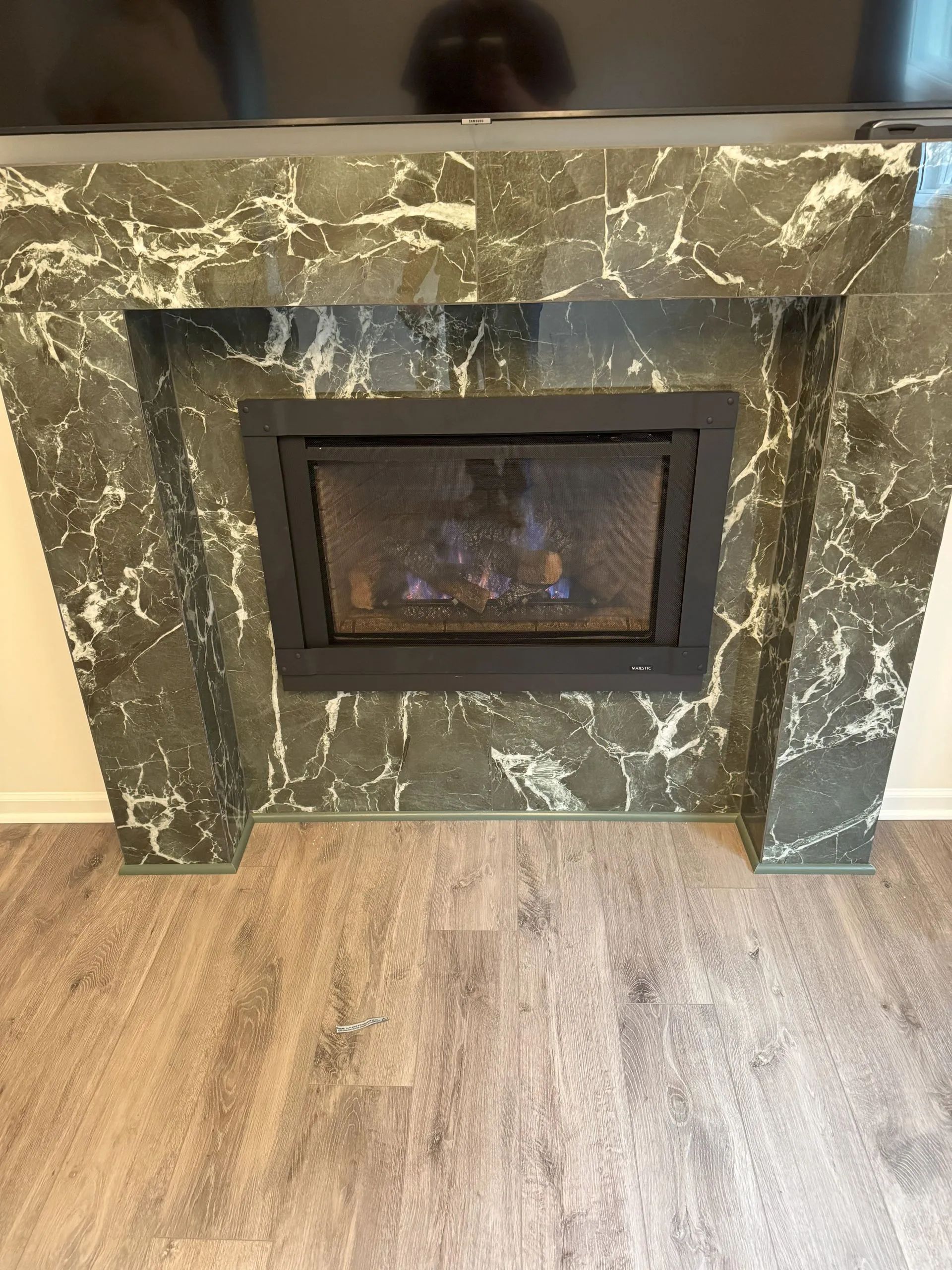 Green marble fireplace with a small glass-front gas insert on a wood floor.