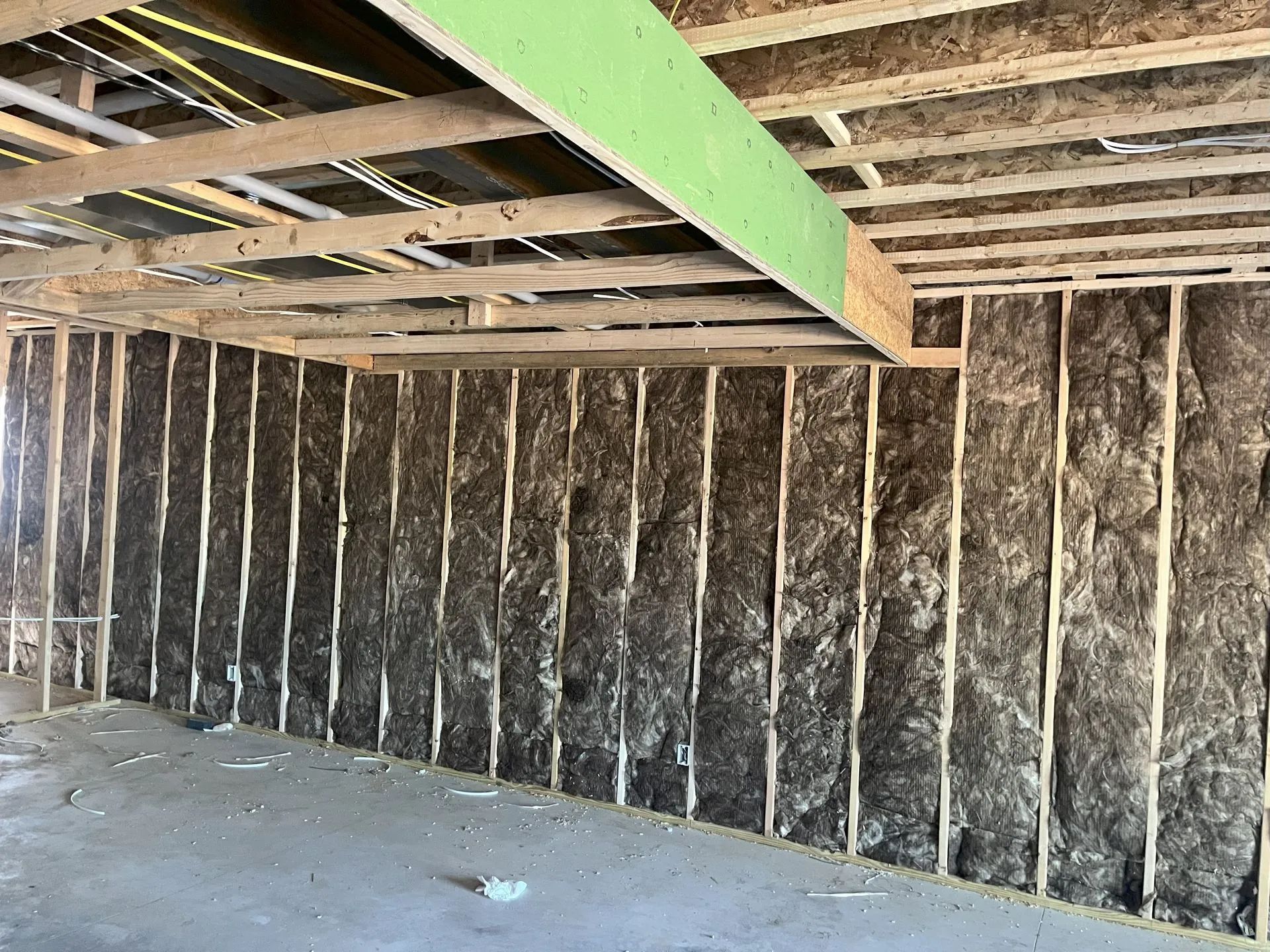 Unfinished basement with exposed wooden ceiling joists, insulation-covered walls, and a concrete floor.