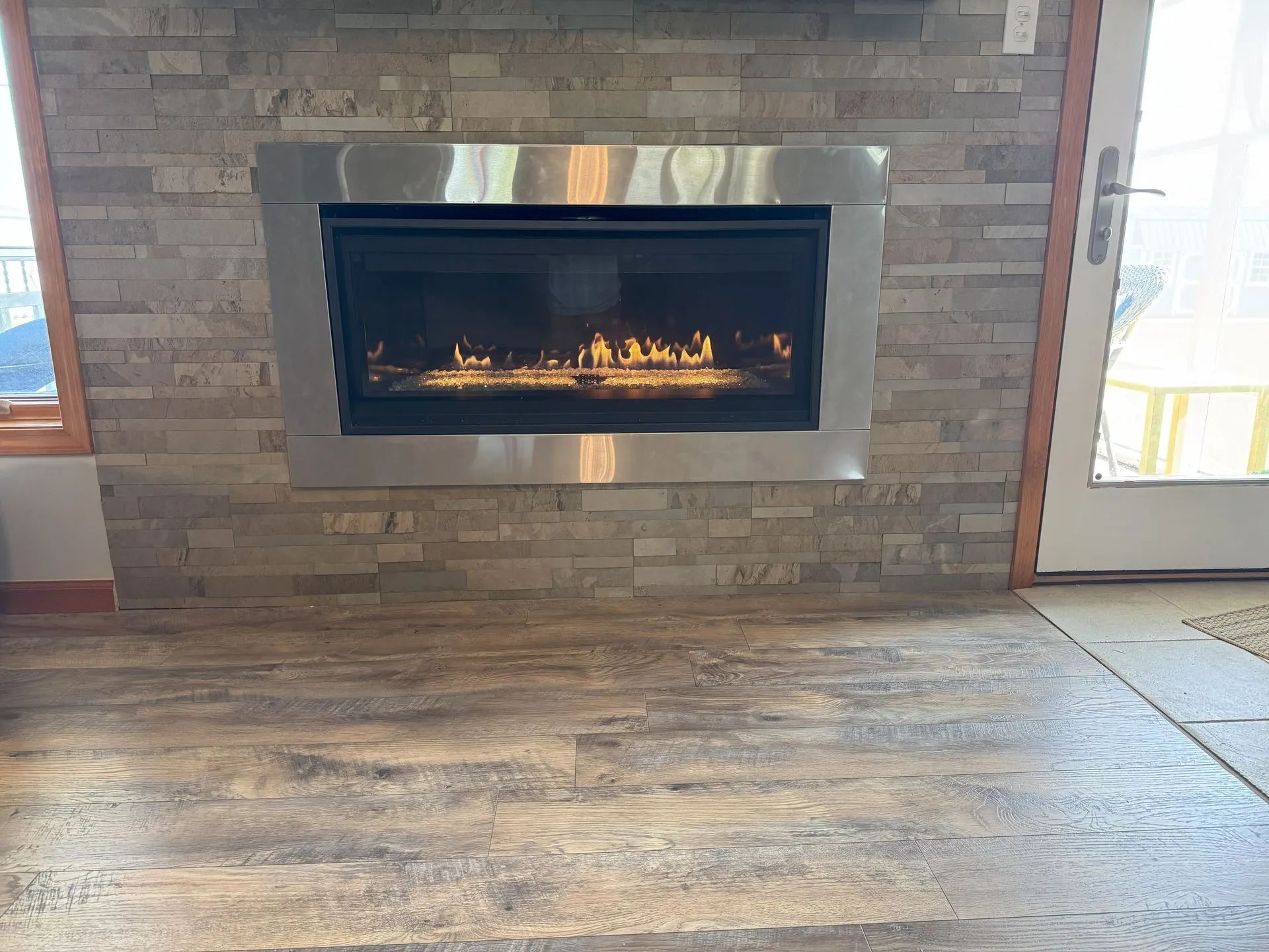 Modern stone fireplace with a lit gas fire in a brick wall and wood-patterned floor in a bright room