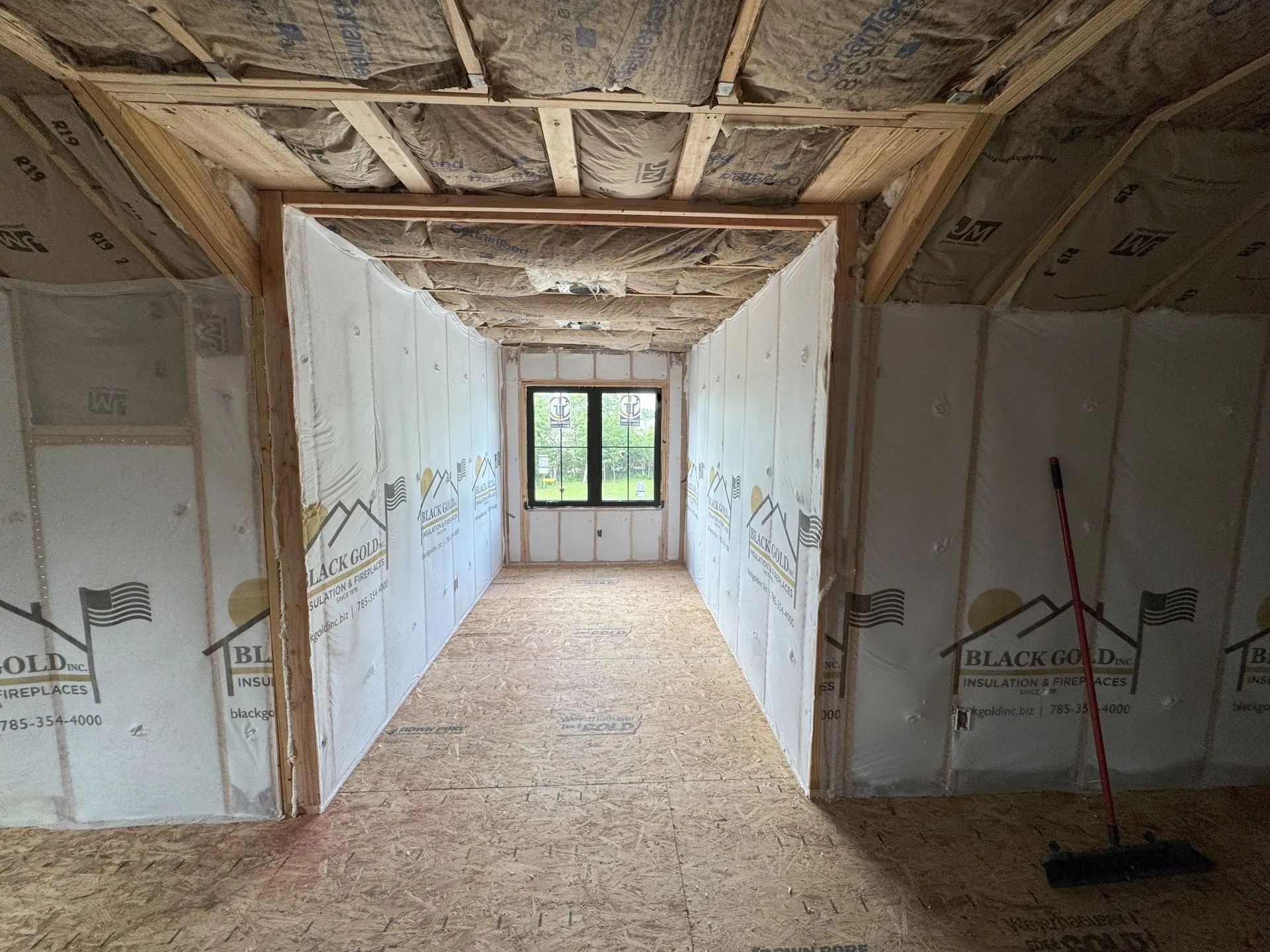 Unfinished hallway with drywall, exposed beams, and a window at the far end.