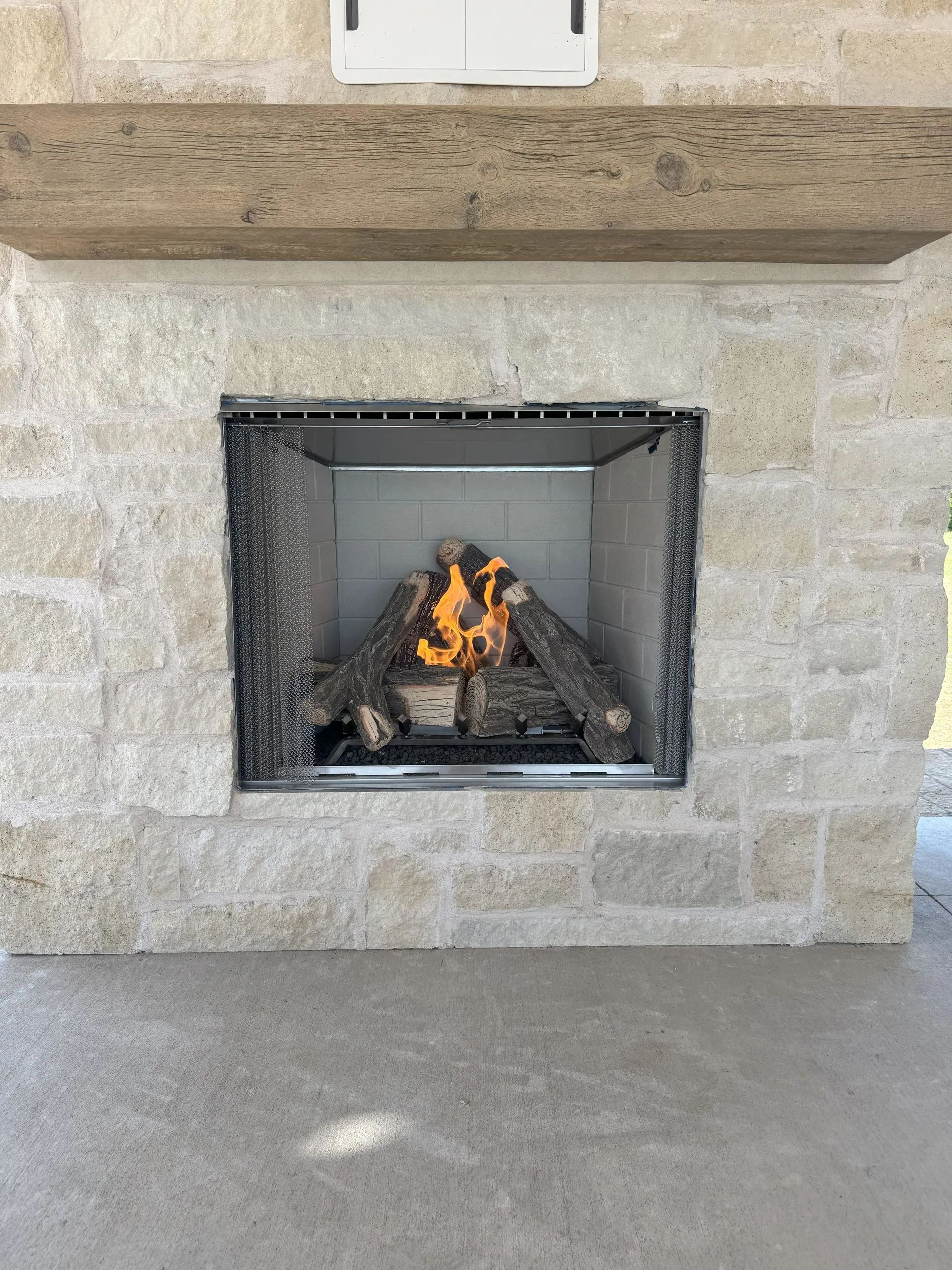 Lit stone fireplace with a small fire burning inside and a gray hearth below.