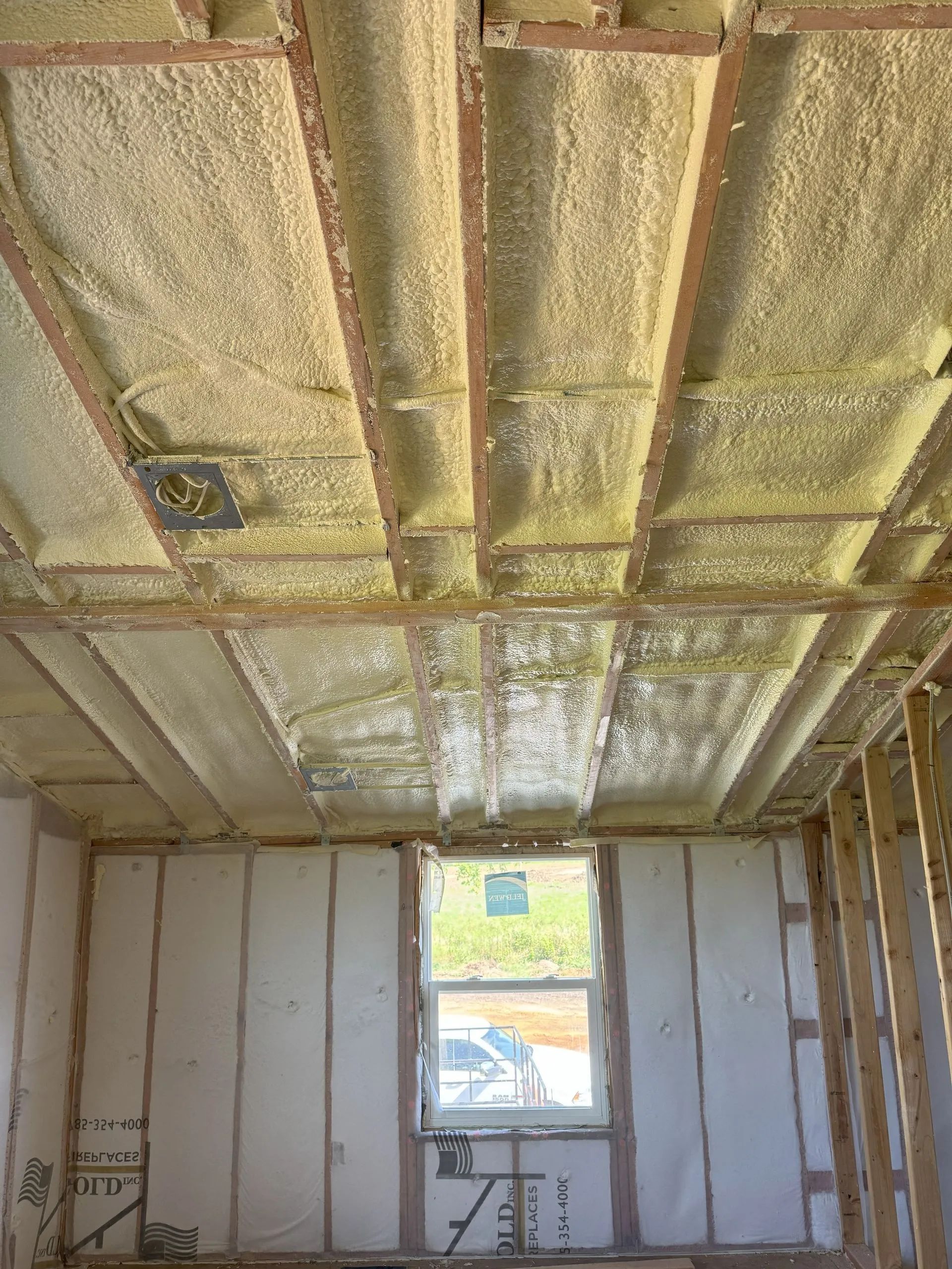 Interior room under renovation with spray-foamed ceiling, exposed framing, and a small window.