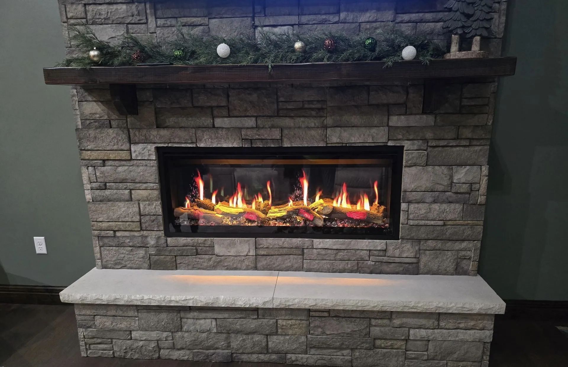 Stone fireplace with a lit gas fire, dark surround, and a mantel with greenery and ornaments