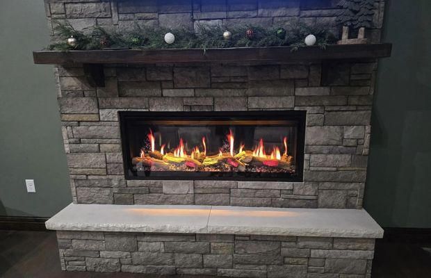 Stone fireplace with a lit gas fire, mantle decor, and a matching stone bench beneath it.