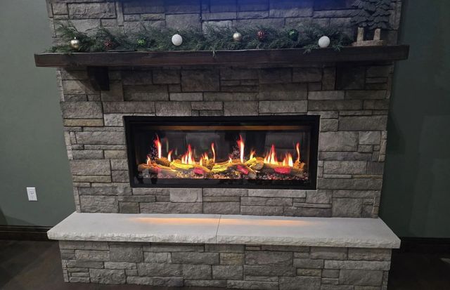Stone fireplace with a lit gas fire, mantle decor, and a matching stone bench beneath it.