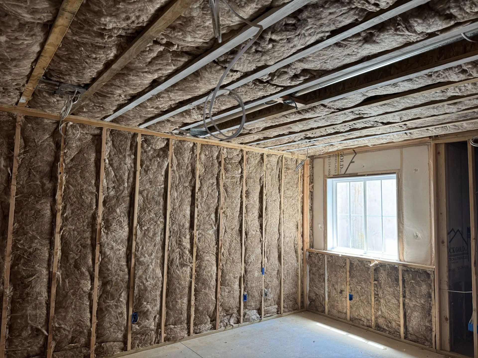 Insulated unfinished room with exposed wall studs, ceiling joists, and a window letting in daylight