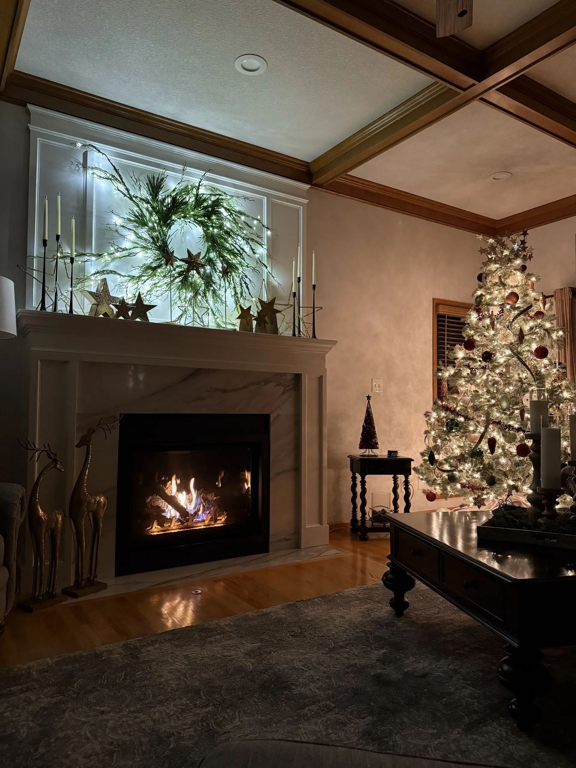 Elegant living room with lit fireplace, Christmas tree, and festive greenery above the mantel