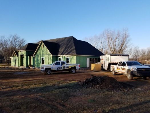 Two trucks are parked in front of a house under construction.