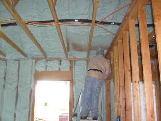 A man is standing on a ladder in a room with foam on the ceiling.