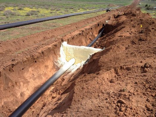 A black pipe is laying in the dirt in a trench.