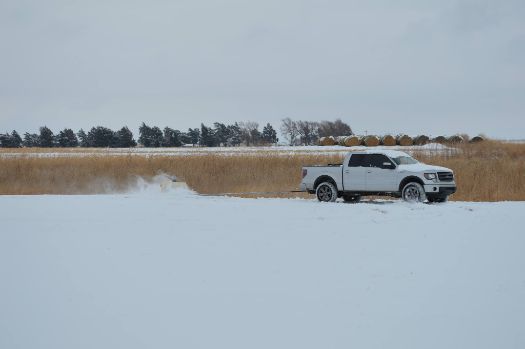 A white truck is driving through a snowy field.