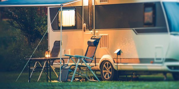 An RV parked in a grassy field with a table and chairs