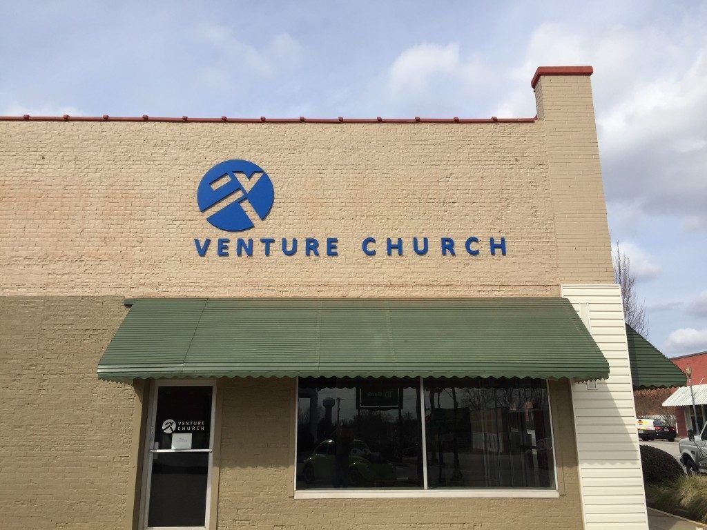 The front of a brick building with a blue sign that says venture church.