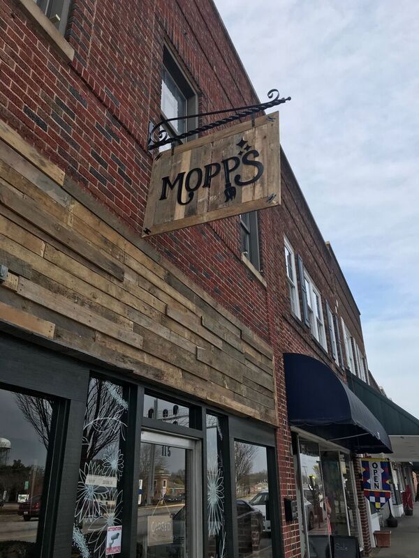 A wooden sign hangs from the side of a brick building.