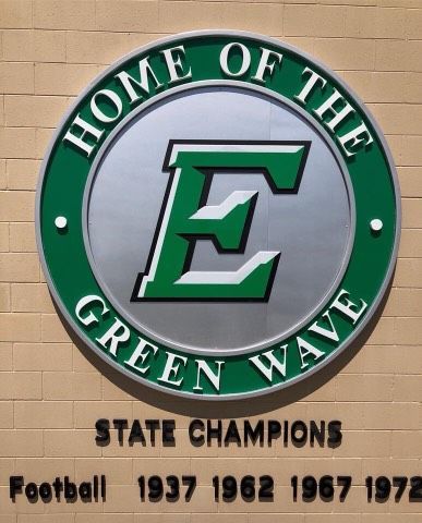 A sign on a brick wall that says home of the green wave