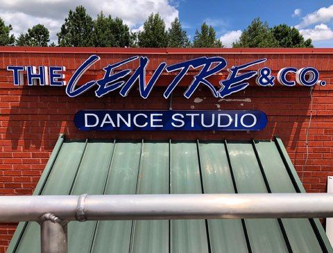 A sign for the centre & co. dance studio is on the side of a brick building.
