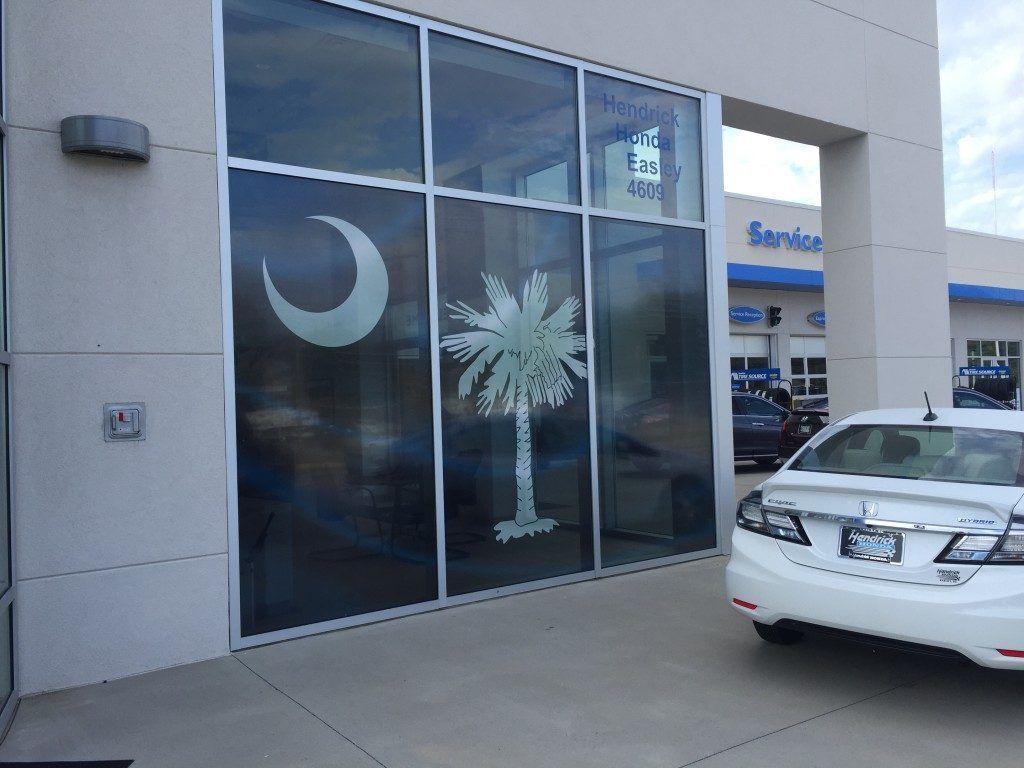 A white car is parked in front of a car dealership