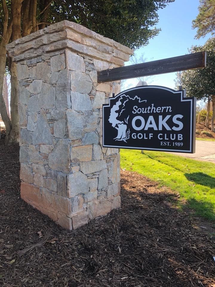 A sign for southern oaks golf club is hanging from a stone pillar.