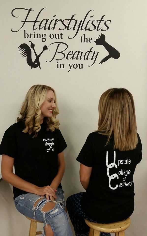 Two women are sitting in front of a wall that says hairstylists bring out the beauty in you