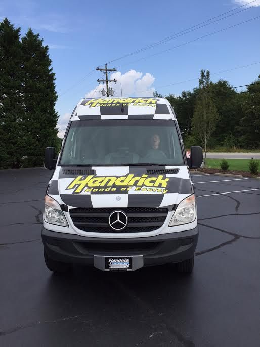A white and black van with the word hendrick on the front is parked in a parking lot.