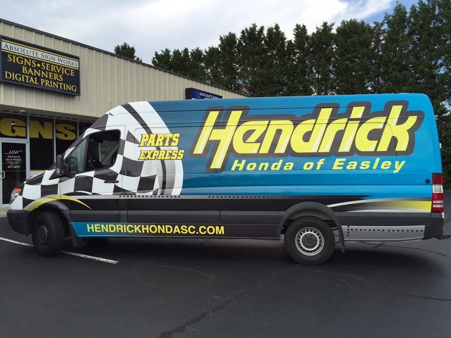 A blue van with the word hendrick on it is parked in front of a building.