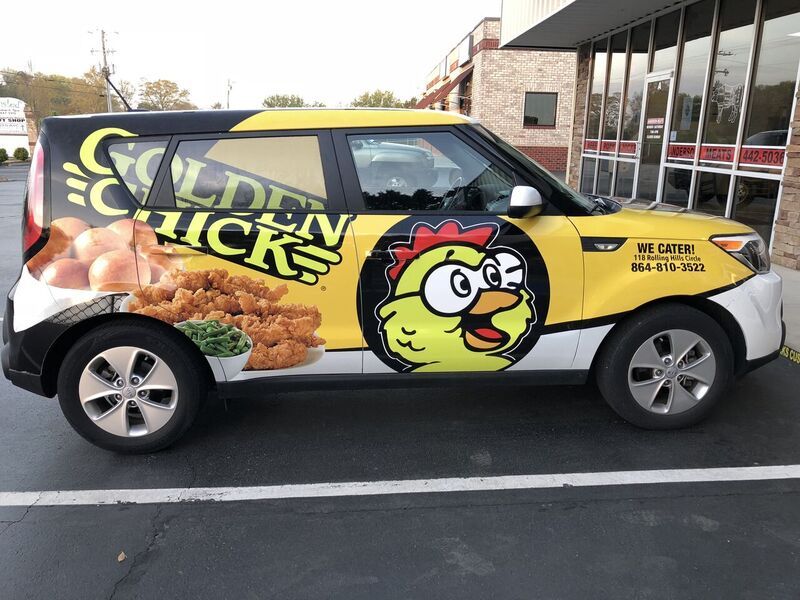 A yellow and black van with a chicken on the side is parked in a parking lot.