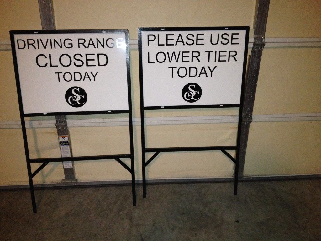 Two signs that say driving range closed today and please use lower tier today