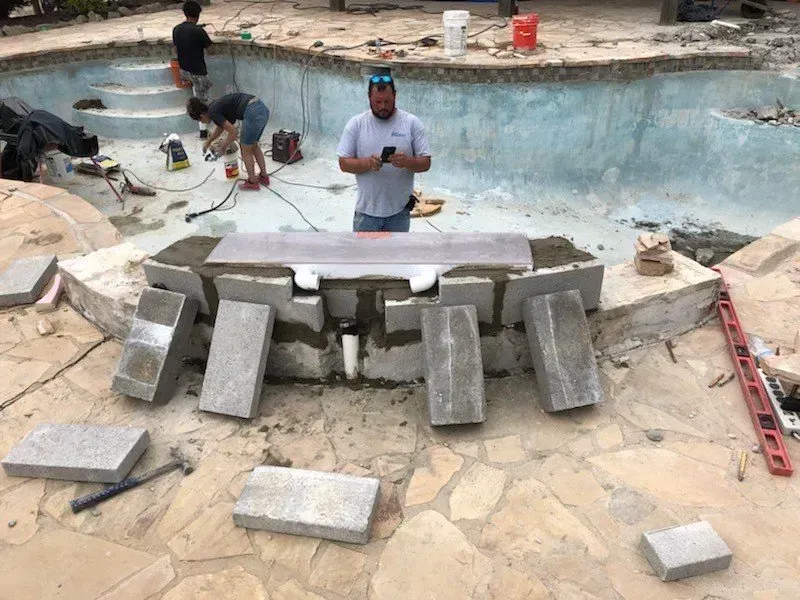 Pool construction: Workers installing stonework around a pool feature; partially constructed pool with tools and materials.
