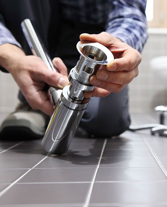 A man is kneeling on the floor fixing a sink faucet.