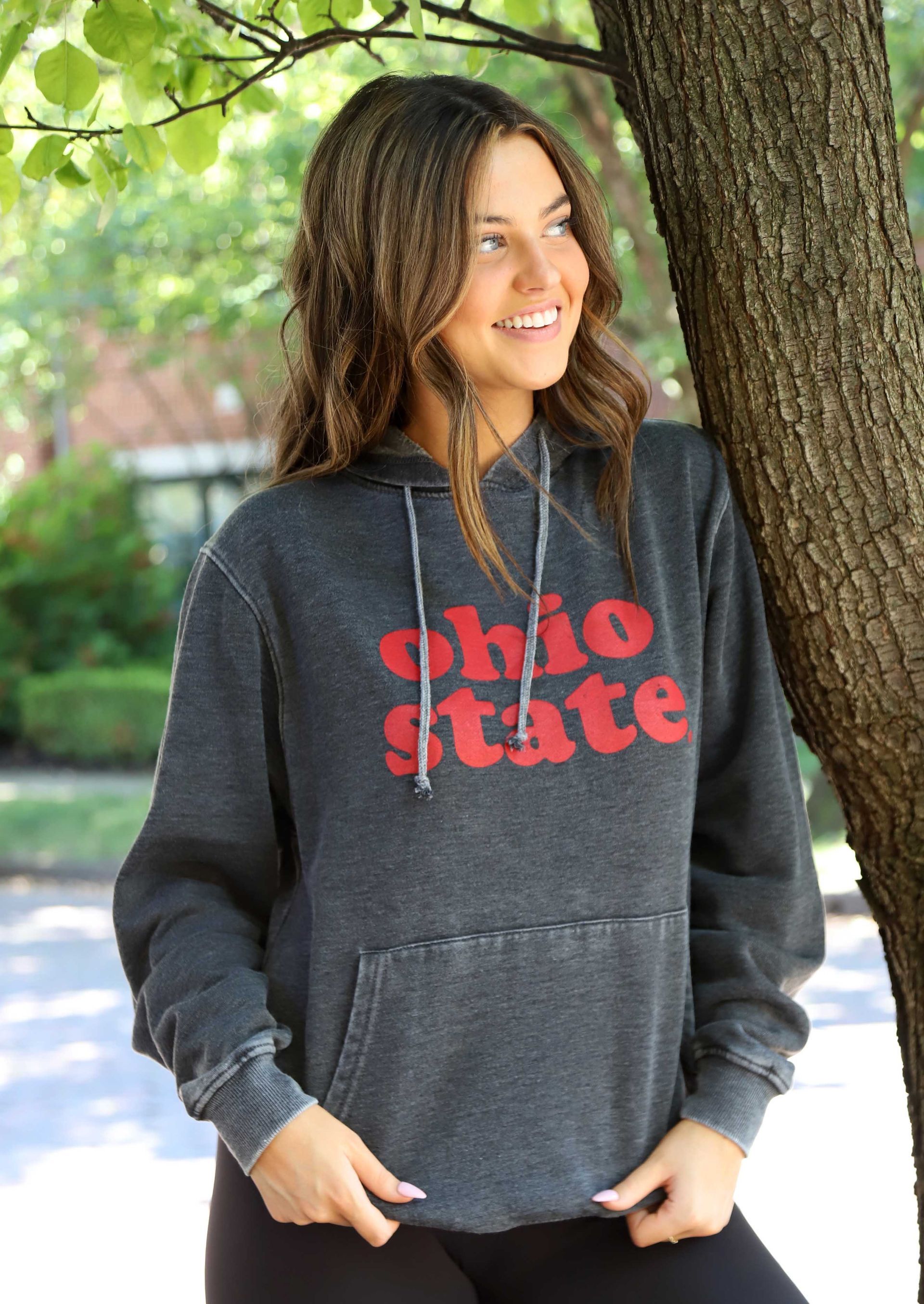 A woman wearing a ohio state hoodie is standing next to a tree.