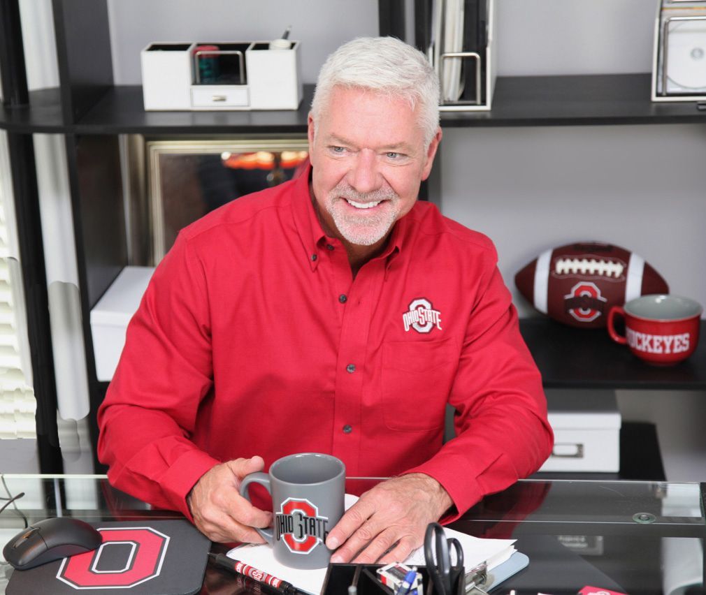 A man in a red ohio state shirt is sitting at a desk