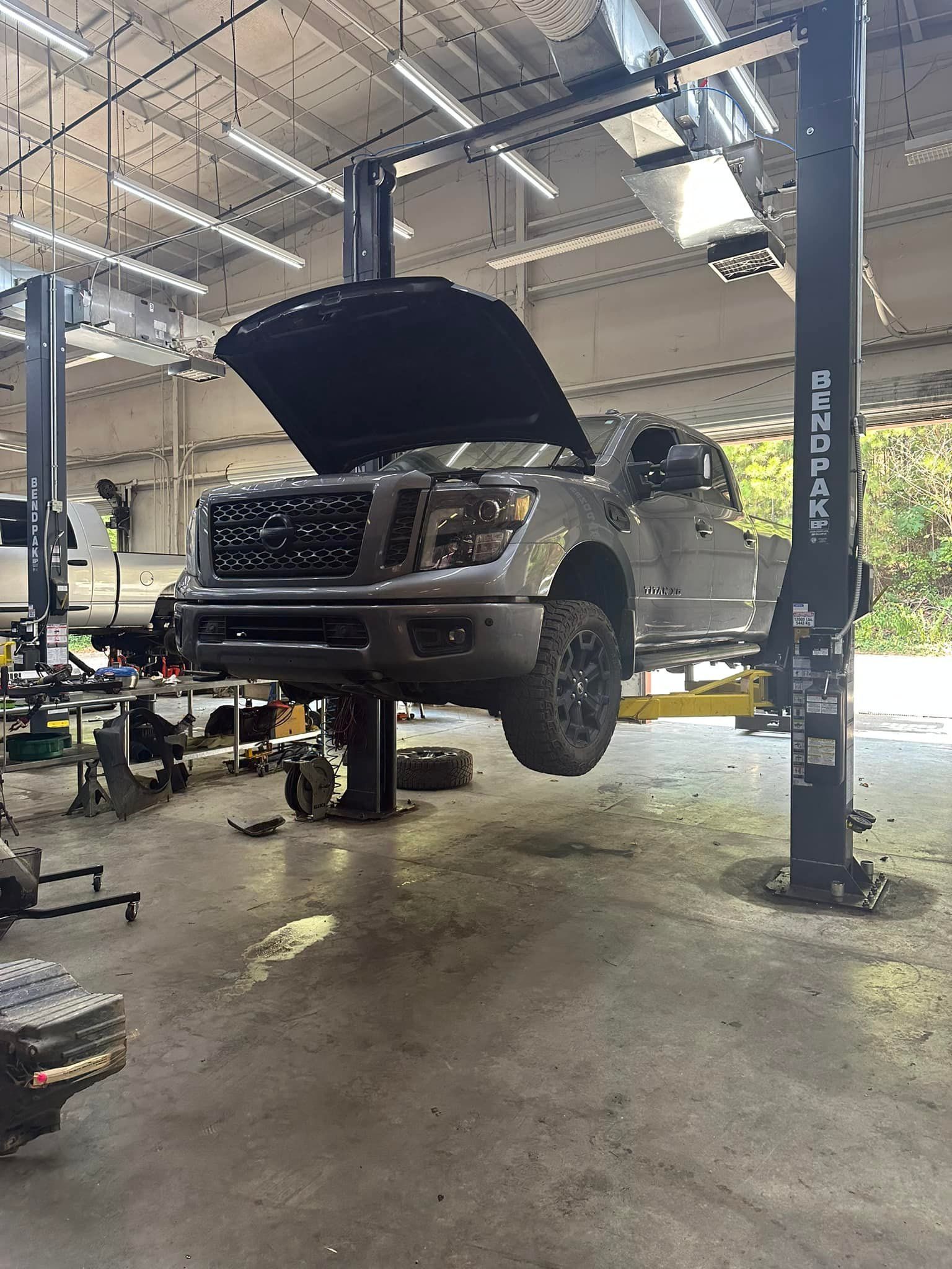 A truck is sitting on a lift in a garage with its hood open.