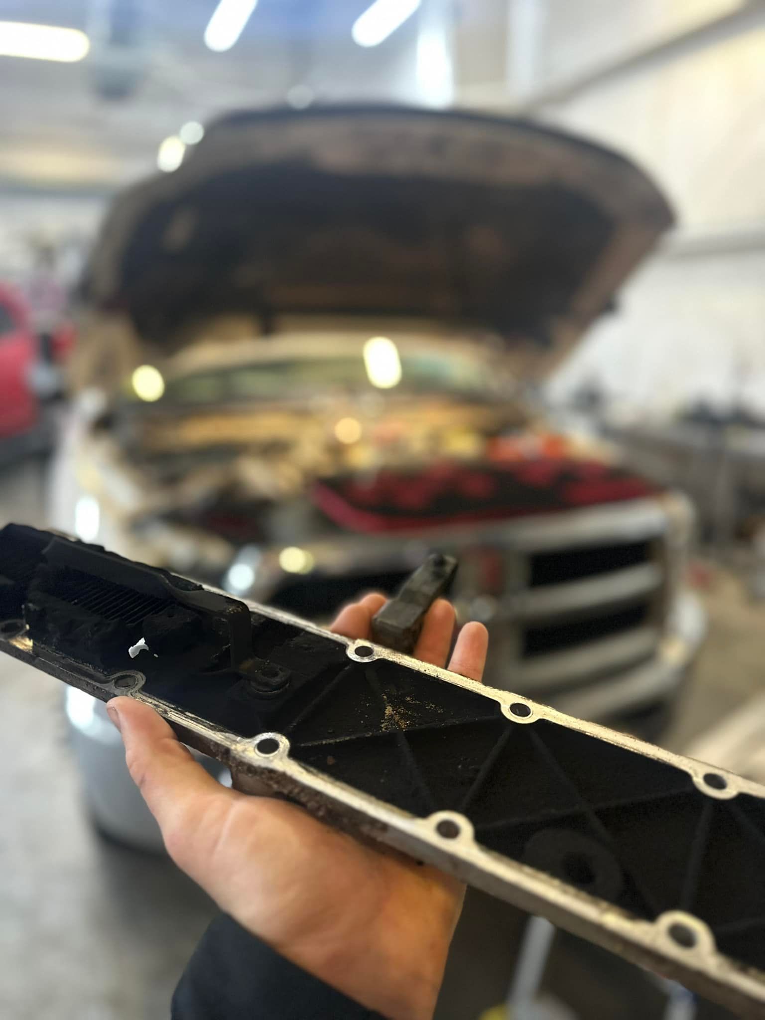 A person is holding a piece of metal in front of a car with the hood open.