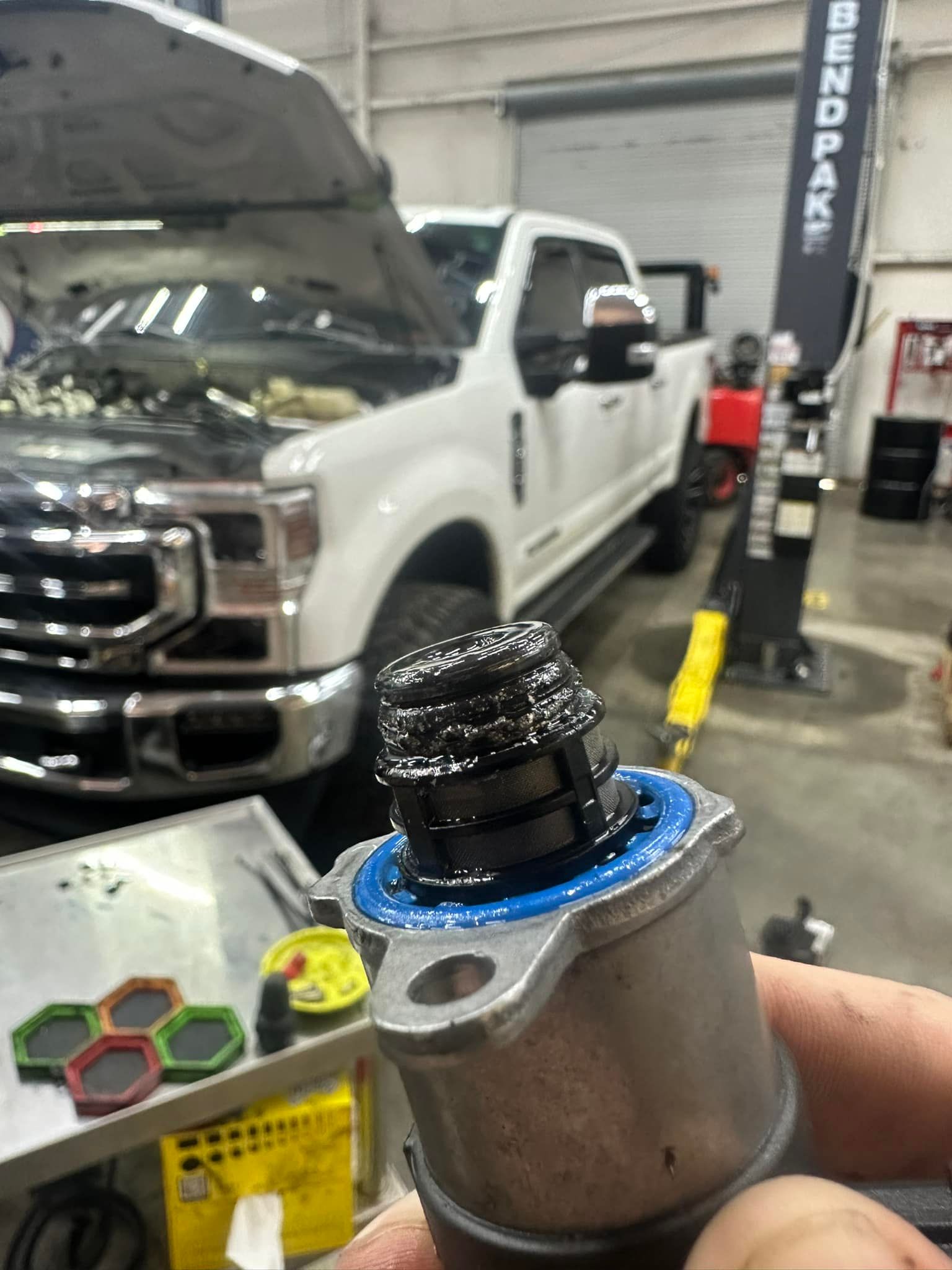 A person is holding a valve in front of a white truck with the hood up.