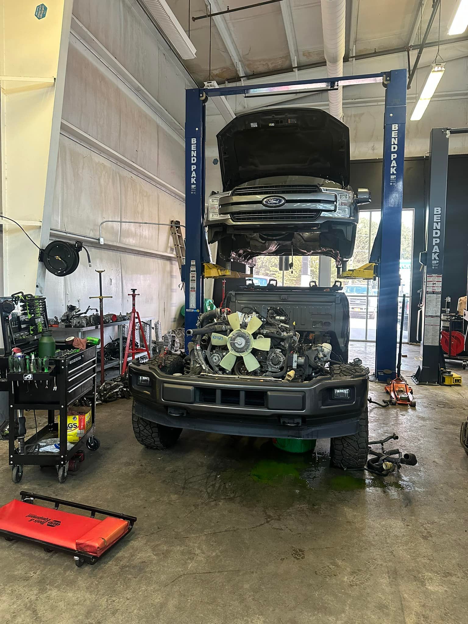 A truck is being worked on in a garage with the hood up.