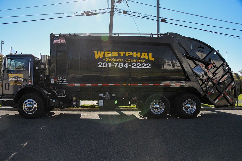 Black Westphal waste truck with phone number parked on asphalt road.