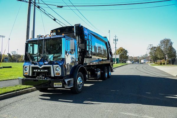 Dark blue Mack garbage truck parked on a street, under a clear sky.