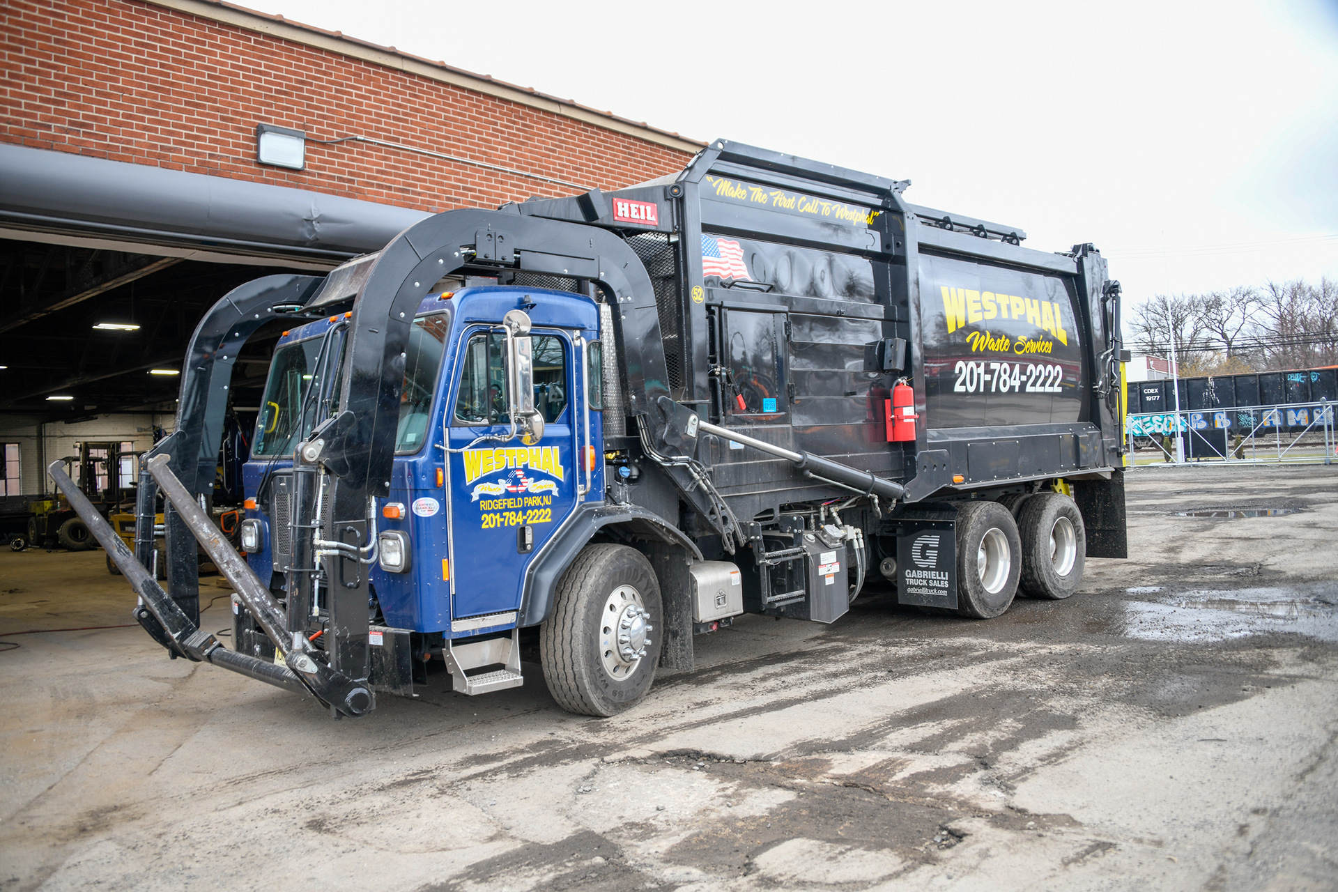 Blue and black garbage truck parked in front of a brick building.