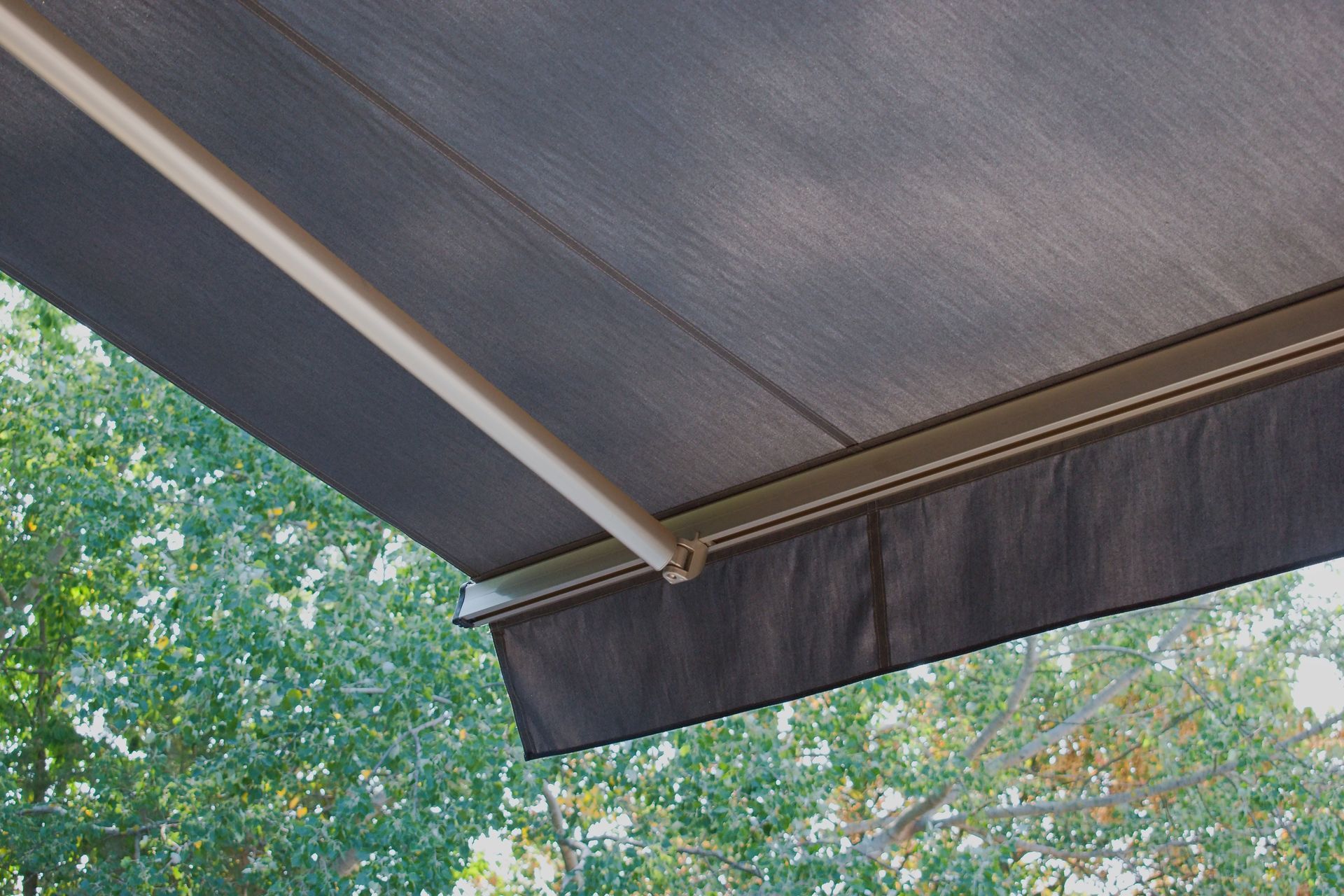 Dark gray retractable awning over outdoor foliage.