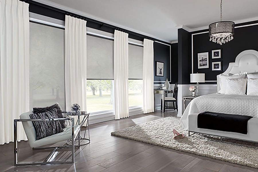 Elegant bedroom with white curtains, roller shades, and a large bed against a dark wall.