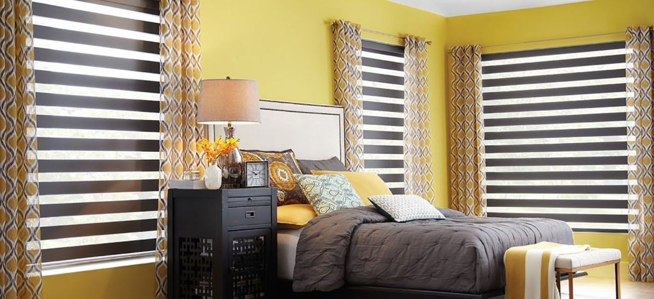 Bedroom with yellow walls, dark blinds, and a gray bed.