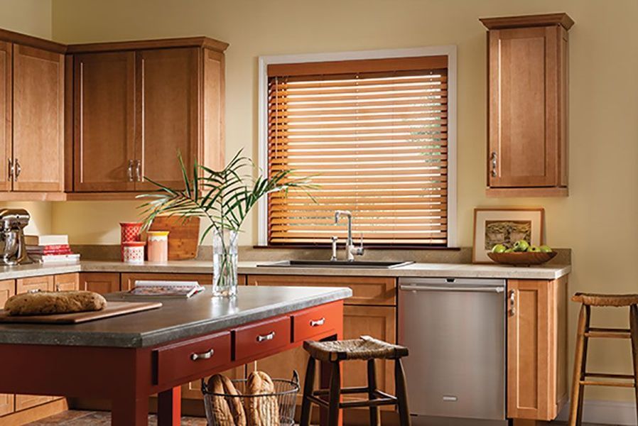 Kitchen with wood cabinets, red island, and stainless steel dishwasher. Window has wooden blinds.